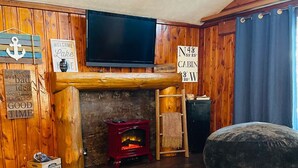A cozy cabin interior with a wooden interior, a fireplace, a television mounted on the wall, and a large cushioned seating area. - Beautiful 2BR+Loft Cottage with amazing views!

 (Beaverton)