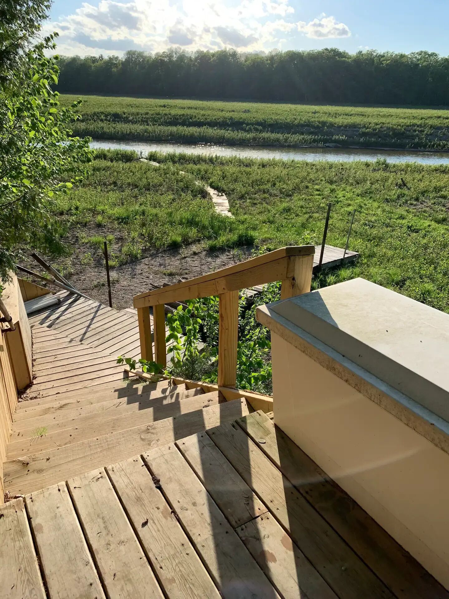 A wooden staircase leading to a deck overlooking a river and a field.