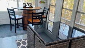 A cozy outdoor seating area with a round table, bar stool, and wicker chairs, overlooking a lake. - Beautiful 2BR+Loft Cottage with amazing views!

 (Beaverton)