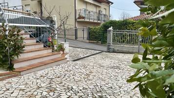 Un quartiere residenziale con un cortile pavimentato, una scala che conduce a un balcone e un ingresso con cancello.