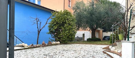 A courtyard with a stone floor, a blue wall, and a building with a beige facade.
