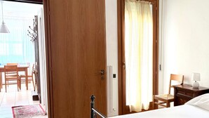 A bedroom with a bed, a wooden door, a window with curtains, a bedside table, and a chair. - S327 - Sirolo, comfortable two-room apartment well equipped (Sirolo)