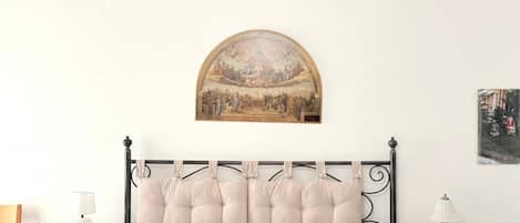 A bedroom with a bed, two nightstands, a wall-mounted painting, and a small table lamp.