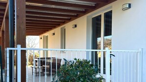 Zona exterior coberta amb barana blanca, taula amb cadires i una planta en test.