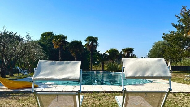 Una piscina amb dues gandules al primer pla i un cel blau i clar.
