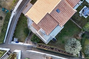 An aerial view of a building with a sloped roof, a fenced yard, and a small garden area.