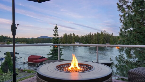 Un foyer extérieur sur une terrasse donnant sur un lac, avec des bateaux et un quai en arrière-plan.