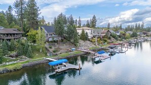 Une propriété au bord du lac, avec des bateaux amarrés, un petit quai surmonté d’un auvent bleu, et des maisons dotées de grandes fenêtres donnant sur l’eau.