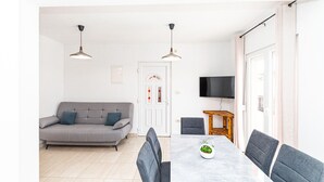 Ett modernt vardagsrum med en grå soffa, ett matbord med grå stolar och en tv som är monterad på väggen.