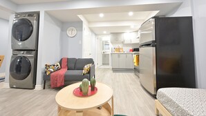 Un apartamento moderno con cocina, comedor y sala de estar. Incluye lavadora, refrigerador, sofá y una pequeña mesa con adornos.