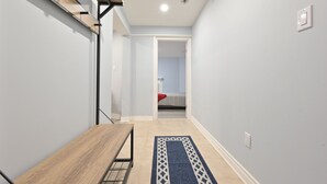 Un pasillo estrecho con un banco de madera, un tapete estampado y una cama en la habitación contigua.