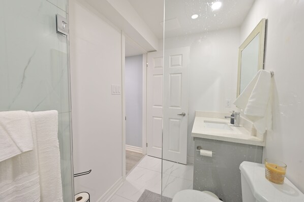 Een moderne badkamer met een douchecabine van glas, een wit wastafelmeubel en een toilet.