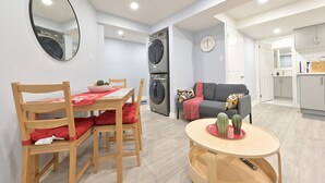 Una sala moderna con comedor, un sofá gris, una mesa redonda con un cactus y un cuarto de lavado con lavadora.