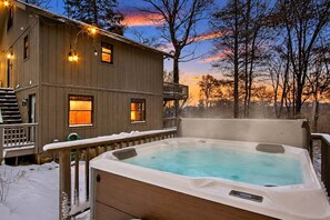Eine Holzblockhütte mit Whirlpool, einer Terrasse und Blick auf Bäume sowie einen Sonnenuntergang.