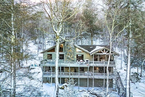 Un chalet à plusieurs étages doté d’un balcon, entouré d’arbres couverts de neige.