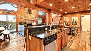 A wooden cabin interior with a kitchen, dining area, and a stone fireplace.
