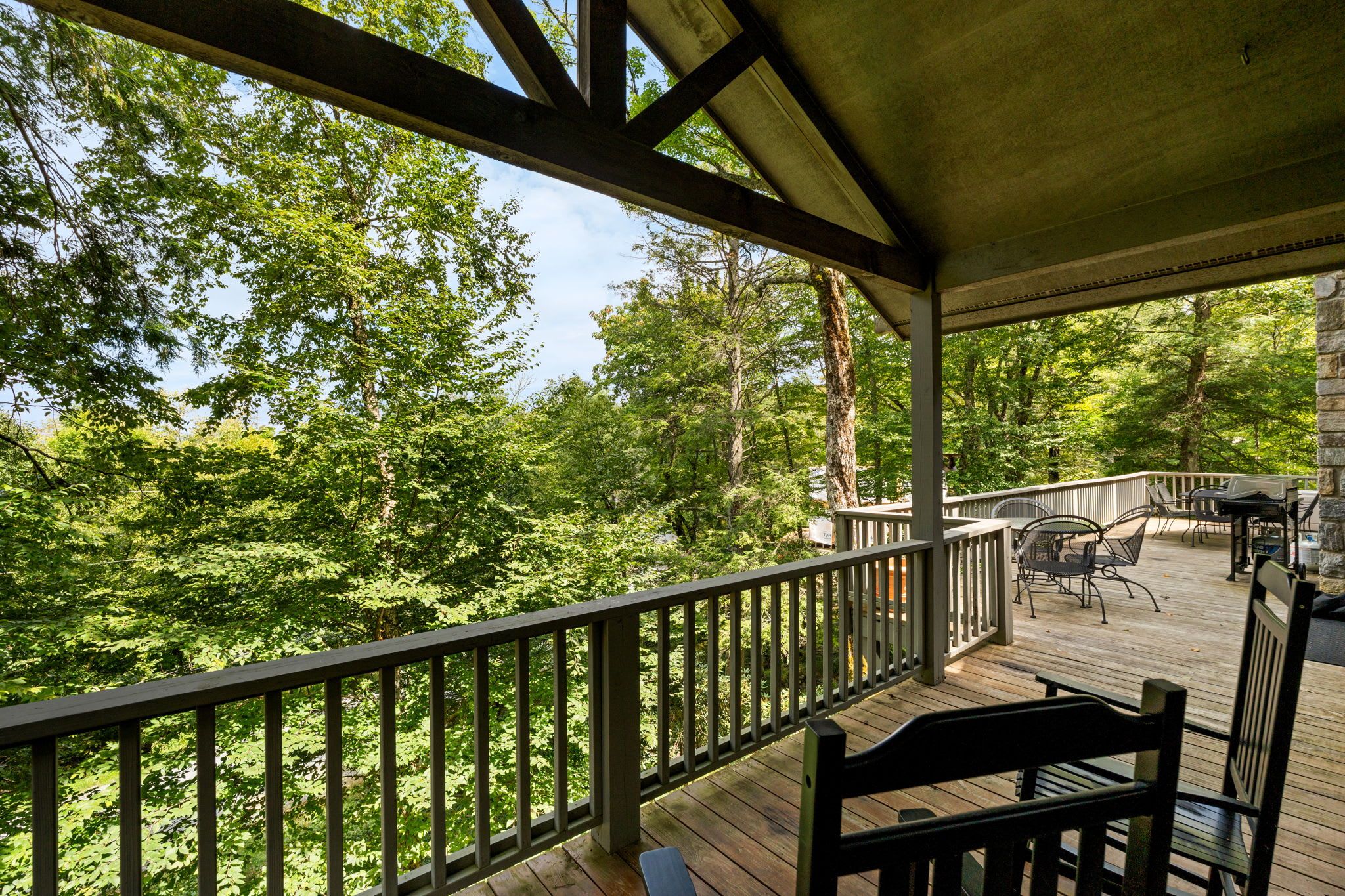A wooden deck with a railing, outdoor furniture, and a view of a forest.