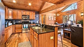 A wooden cabin interior with a kitchen, dining area, and a large window.