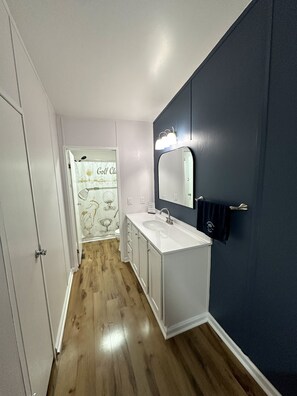 Casa de banho com toucador branco, um espelho grande e uma parede de destaque azul escuro.