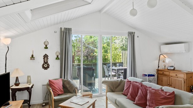 A spacious living room with a large sliding glass door leading to an outdoor patio, a wooden dining table, and a cozy seating area with a sofa and armchairs. - 3 bedroom beautiful home in Væggerløse (Væggerløse)