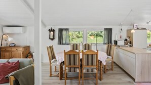 A spacious room with a dining table set for four, wooden chairs, a kitchen area with a microwave, and a large window providing a view of greenery outside. - 3 bedroom beautiful home in Væggerløse (Væggerløse)