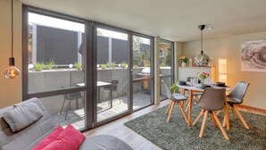A modern living room with a sofa, a dining table with chairs, and a kitchen area visible through large sliding glass doors. - Ferienwohnung in Luxusvilla (Bahrdorf)