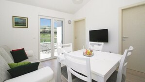 Ein modernes Wohnzimmer mit einem weißen Sofa, einem Esstisch mit Stühlen, einem Flachbildfernseher und einer Glastür zum Außenbereich.
