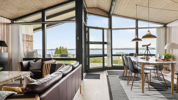 Ein modernes Interieur mit großem Fenster, einem Essbereich und einer Sitzecke mit Blick auf das Wasser.