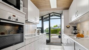 Eine moderne Küche mit weißen Schränken, einem Siemens-Ofen und Blick durch eine offene Tür in einen Garten.