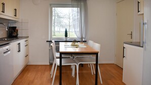 Eine moderne Küche mit weißen Schränken, einem Holztisch und einem Fenster mit Blick auf Bäume.