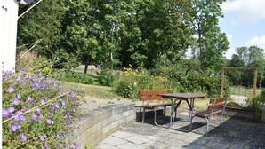 Ein Sitzbereich im Freien mit einem Tisch und zwei Bänken, umgeben von Grünpflanzen und Blumen.