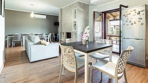 Un salon moderne avec un canapé gris, une table à manger avec des chaises et un coin cuisine équipé d’un réfrigérateur.