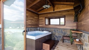 Une cabane en bois dotée d’un jacuzzi, de murs en pierre, d’une petite fenêtre et offrant une vue sur une piscine et la verdure.