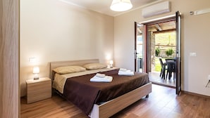 Une chambre à coucher avec un lit en bois, des lampes de chevet, une table de nuit et une vue sur une terrasse extérieure avec une table et des chaises.