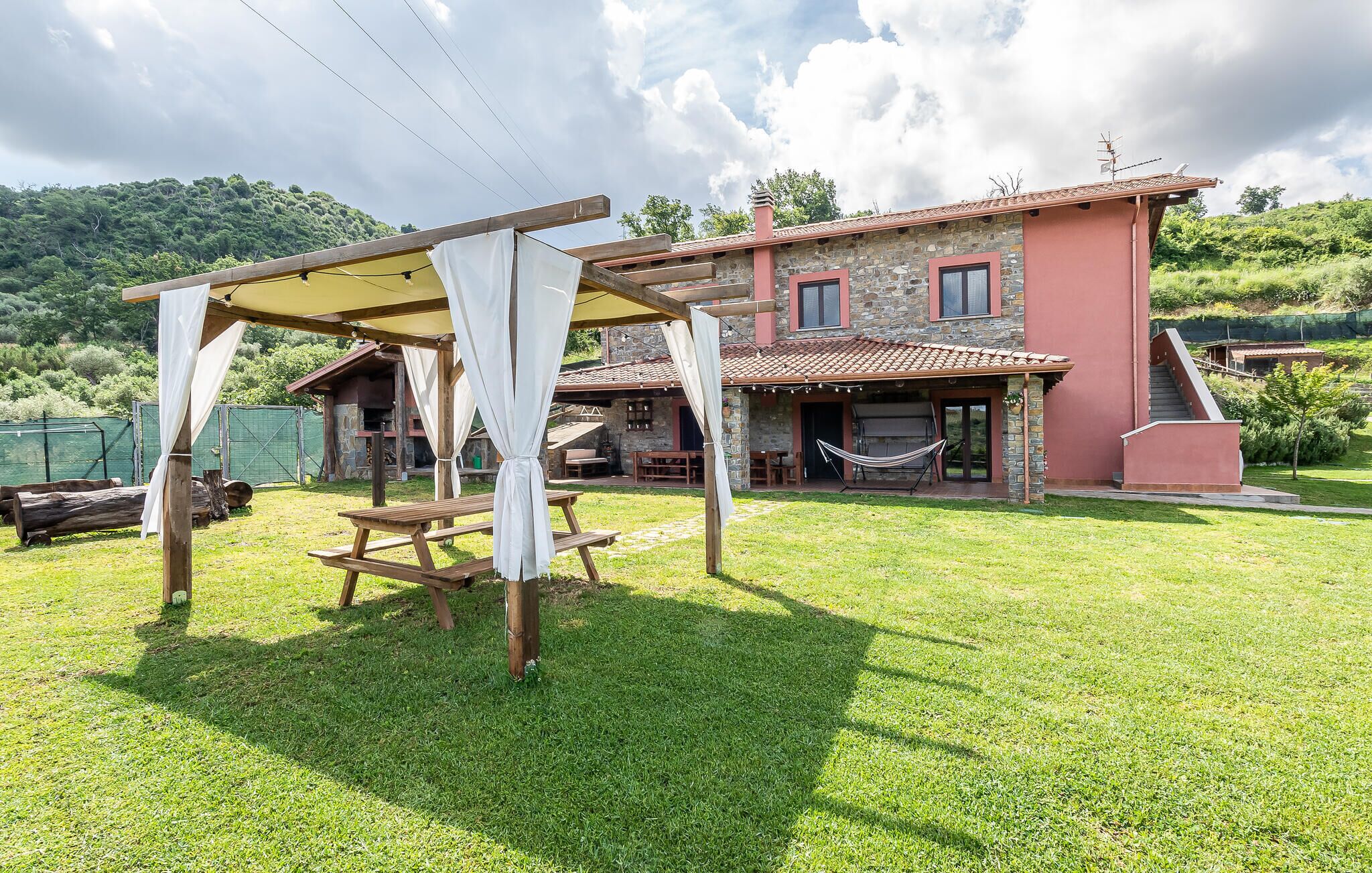 Ein rustikales Steinhaus mit rotem Dach, einer Holzpergola und einer Hängematte.