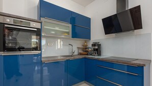 A modern kitchen with blue cabinets, a built-in oven, a coffee machine, and a flat-screen TV mounted on the wall.