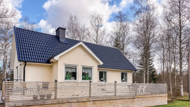 Une maison de plain-pied avec un toit recouvert de tuiles sombres, une cheminée et une clôture en bois.