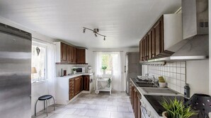 Une cuisine avec des meubles blancs, un réfrigérateur en acier inoxydable, un four à micro-ondes et une cuisinière. Une fenêtre offre une vue sur la verdure à l’extérieur.