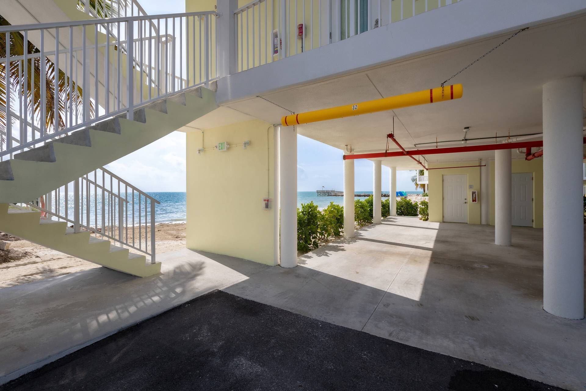 Un espacio al aire libre cubierto con una escalera que conduce a una playa, una manguera contra incendios amarilla y un muelle al fondo.