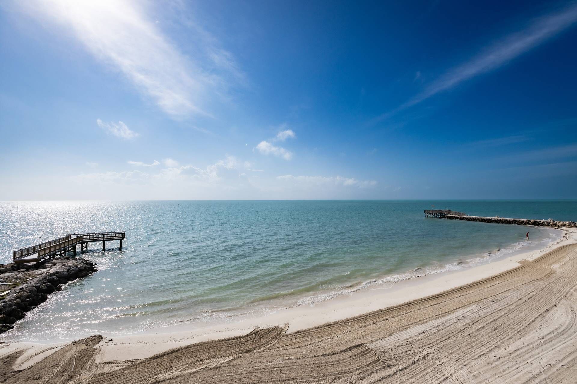 Une plage avec une jetée en bois qui s’avance dans la mer, un ciel dégagé et une eau calme.