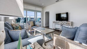 Un vaste espace de vie agrémenté d’un ventilateur de plafond, d’un téléviseur à écran plat posé sur une console en bois et d’un balcon avec mobilier d’extérieur.