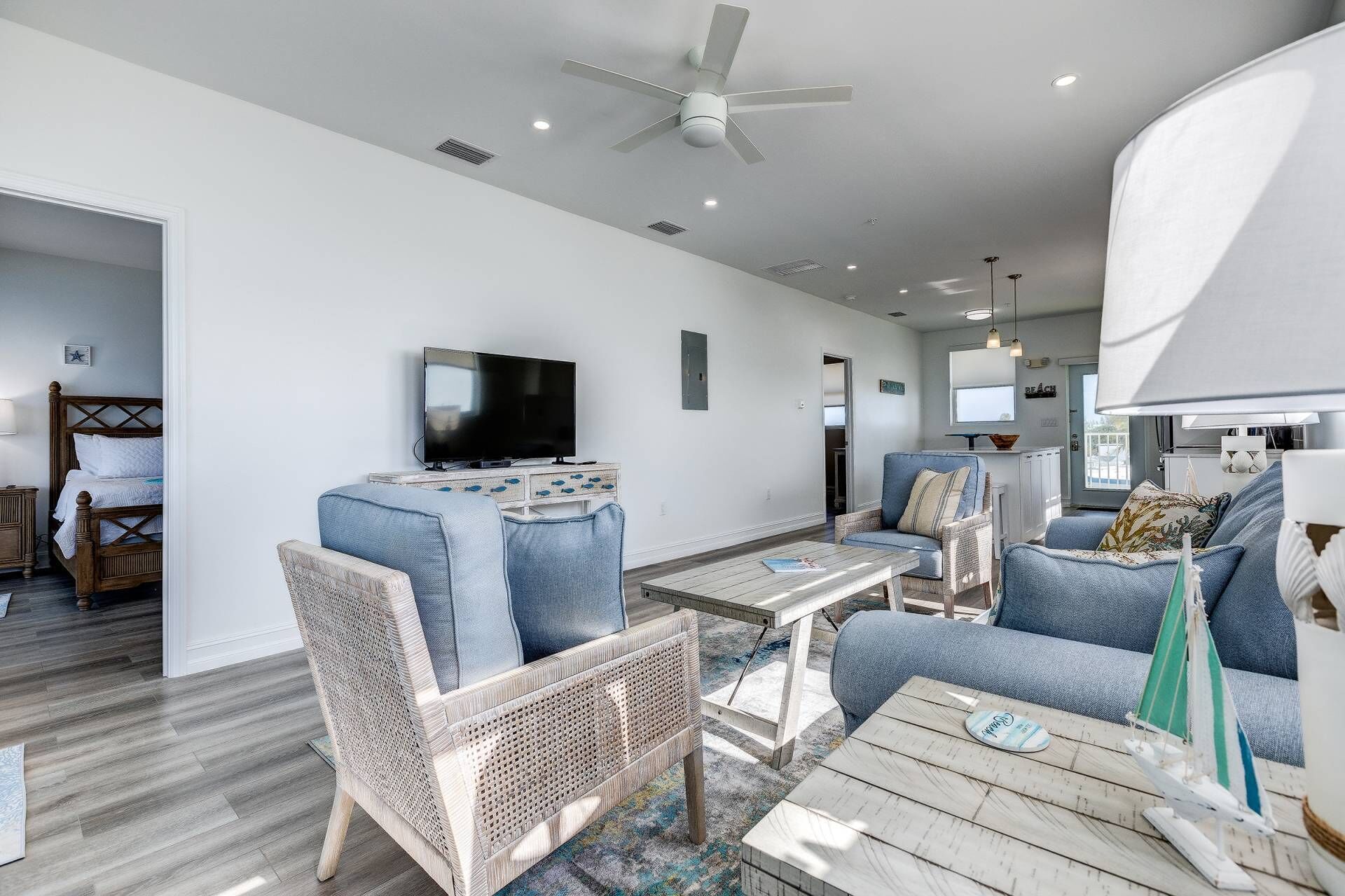 A modern living room with a flat-screen TV, wicker furniture, and a ceiling fan.