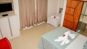 Quarto de hotel com cama, televisão, escrivaninha e guarda-roupa.