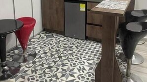 A compact kitchen with a microwave, sink, and a small refrigerator. There are two chairs and a table with a patterned tablecloth. - Cozy apartment in Laureles cool with Air/Acond. (Medellín)