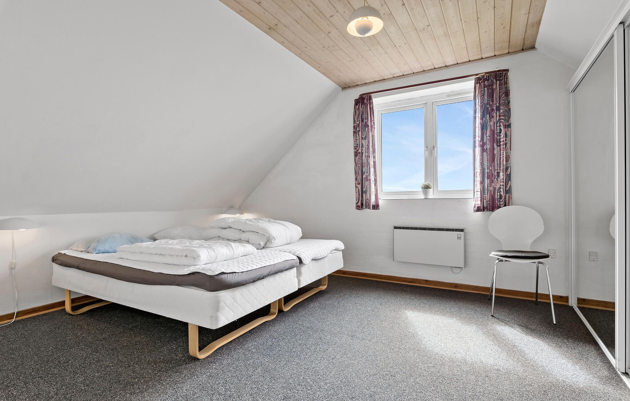 A bedroom with a bed, a radiator, a window with curtains, a chair, and a ceiling light.