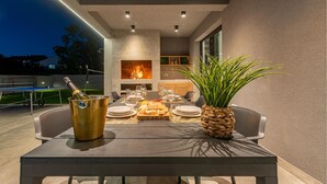 Un espace extérieur aménagé pour les repas, avec une table dressée pour quatre personnes, une bouteille de champagne dans un seau doré et une plante en pot.
