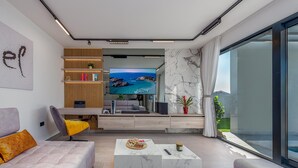 Un salon moderne avec une grande télévision, un canapé, une table basse et un balcon avec vue.