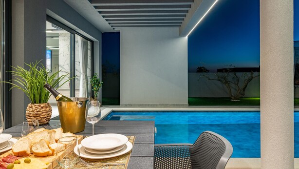 Un espace piscine intérieur moderne, aménagé avec un coin repas comprenant une table, de l’assiette, des verres et une bouteille de champagne.