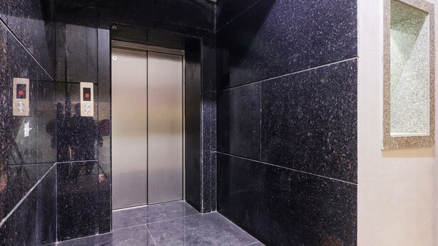A modern elevator with a metallic finish, flanked by black marble walls and a small decorative panel. - FabHotel Rayplus (New Delhi)