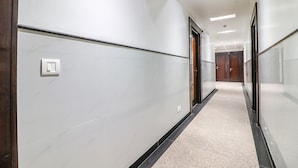 A modern hallway with white walls, a black baseboard, and a light-colored carpet. - FabHotel Rayplus (New Delhi)